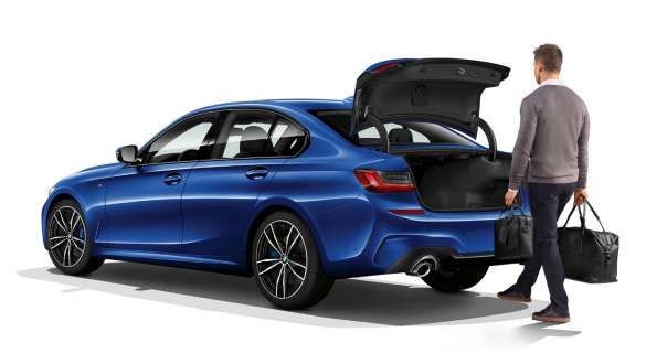 BMW 3 Series Saloon (G20), automatic tailgate operation. Three-quarter rear shot of standing BMW 3 Series Saloon (G20) with driver automatically opening the tailgate with his foot.