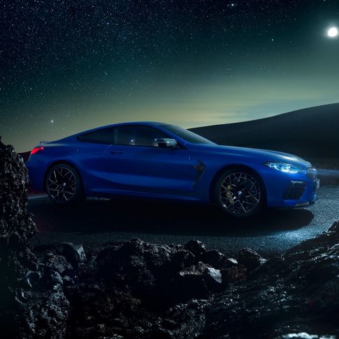 BMW M8 Competition Coupé, three-quarter side view. BMW M8 Competition Coupé in Marina Bay Blue metallic, standing three-quarter side view at night.