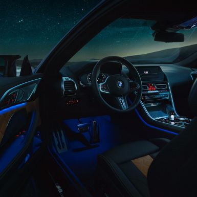 Interior BMW M8 Competition Coupé. BMW M8 Competition Coupé, interior at night with M leather steering wheel and blue ambient light with open driver door.