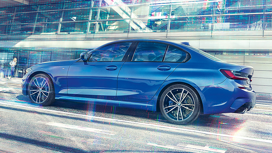 BMW 3 Series Saloon (G20) during the day in front of building made of glass. Static side view of the BMW 3 Series Saloon (G20) Portimao Blue during day in front of building made of glass.