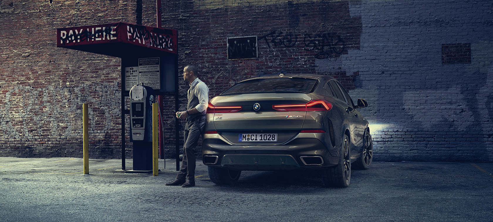 Man leaning on BMW X6. Man leaning on BMW X6 in lateral perspective in front of an urban setting.