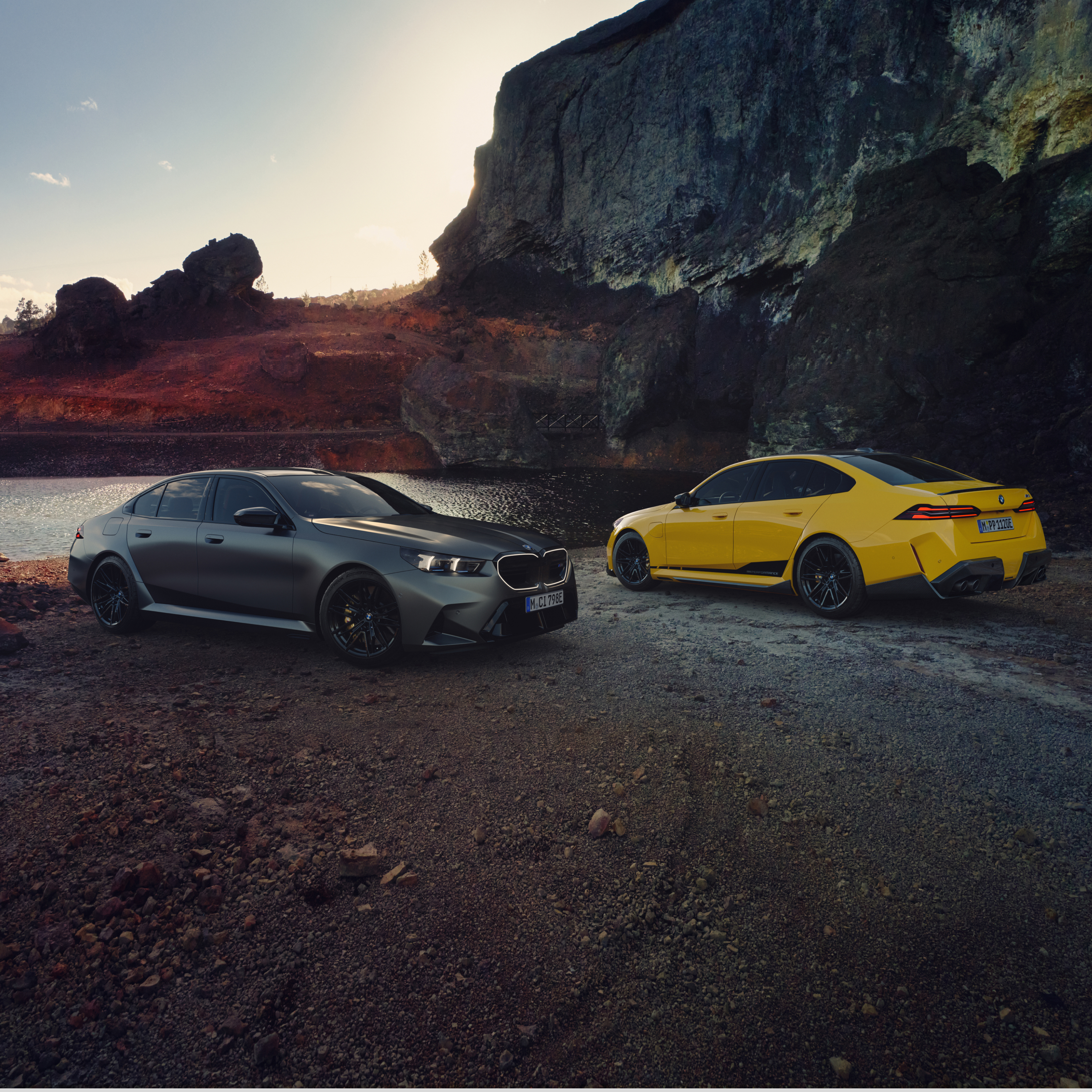 Two BMW 5 Series cars parked on the beach in front of a rock face
